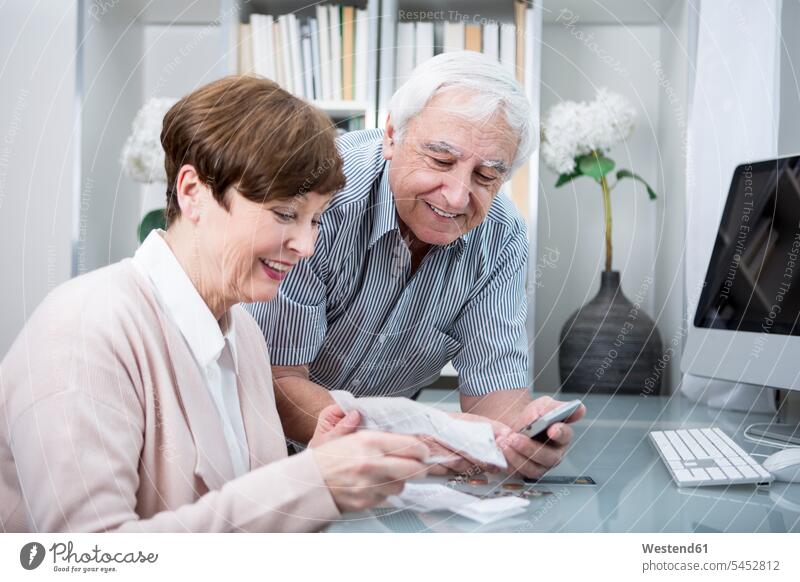 Senior couple with bills and calculator checking their expenses costs Expense online shopping on-line shopping senior adults seniors old saving save calculating