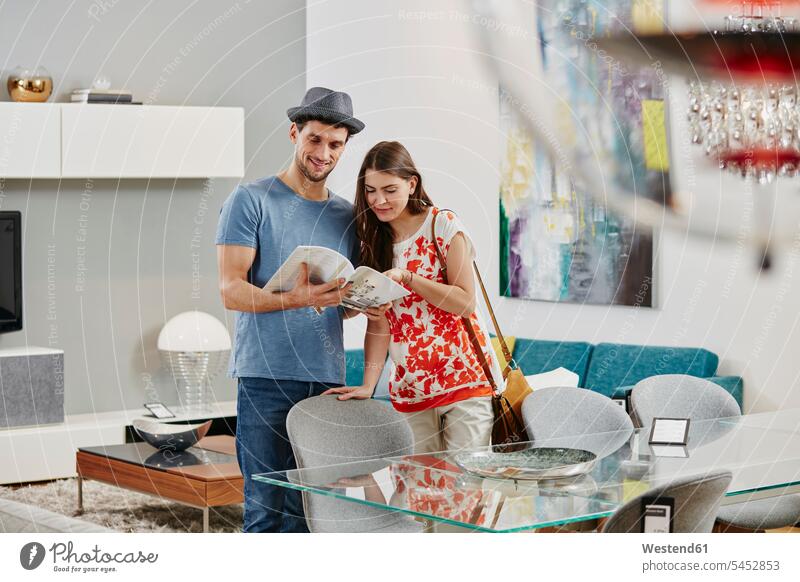 Couple in furniture store looking at dining table, looking at catalogue couple twosomes partnership couples shopping Dining Table Dinner Table Dining Tables