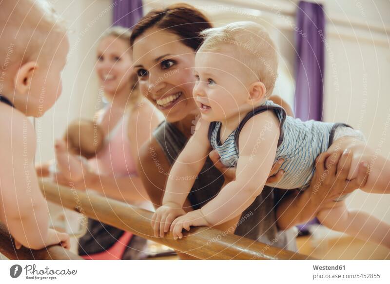 Mother holding up her baby to barre in dance studio mirror mirrors exercising exercise training practising smiling smile barres Fun having fun funny infants