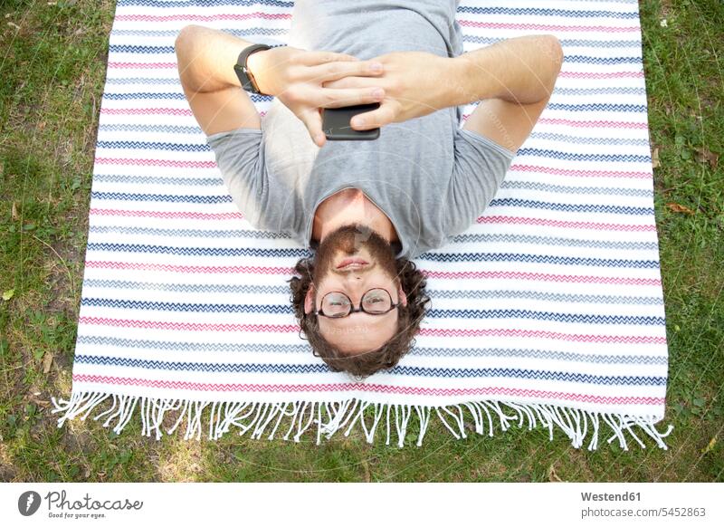 Man lying on blanket in a park using cell phone, top view Smartphone iPhone Smartphones man men males mobile phone mobiles mobile phones Cellphone cell phones
