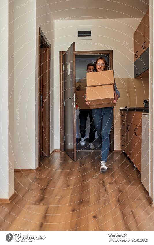 Young women and man carrying cardboard boxes into a room Cardboard Carton carton Cardboards cartons rooms domestic room domestic rooms males friends mate Adults