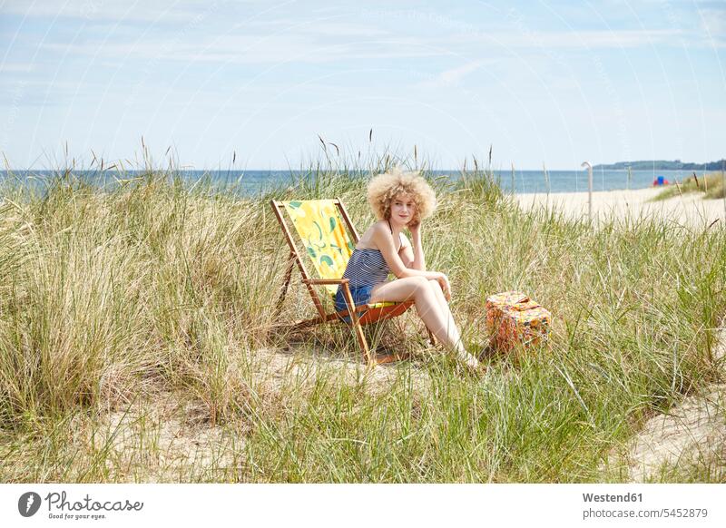 Young woman sitting on beach chair in the dunes watching something females women beachchair beach chairs beachchairs beach dune beach dunes Adults grown-ups