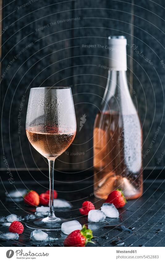 Glass of cooled rose wine, bottle, icecubes and strawberries and raspberries on dark ground ice-cooled iced wet wetness focus on foreground
