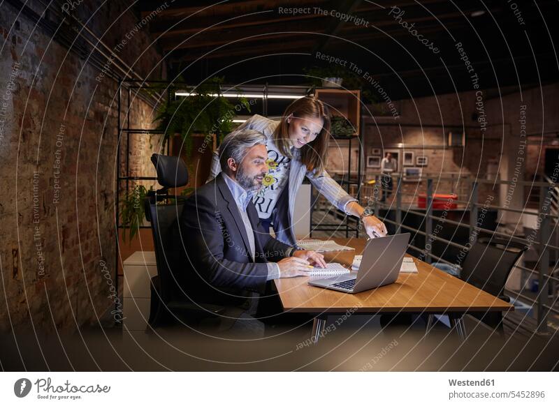 Businessman and woman sitting in modern office, looking at laptop desk desks Seated offices office room office rooms working At Work Laptop Computers laptops