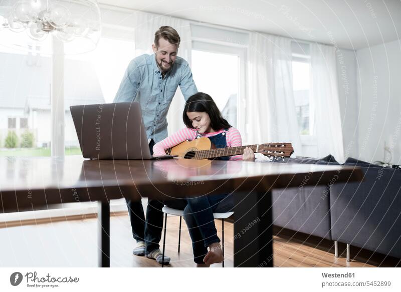 Father smiling at daugher playing guitar in front of laptop Laptop Computers laptops notebook guitars daughter daughters smile father pa fathers daddy dads papa