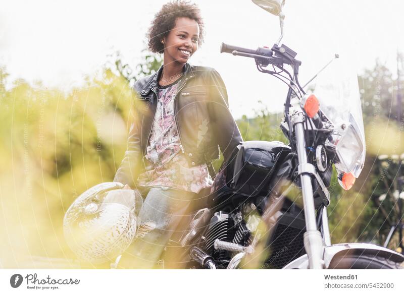 Smiling young woman with her motorcycle females women smiling smile motorbike Motor Cycle Adults grown-ups grownups adult people persons human being humans