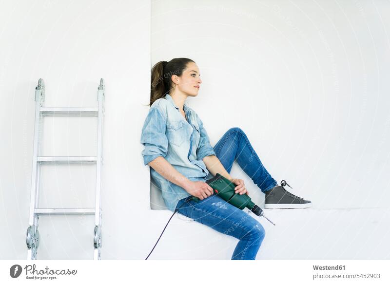 Woman sitting in a niche at ladder holding electric drill woman females women moving house move Moving Home power drill electric drills ladders Adults grown-ups