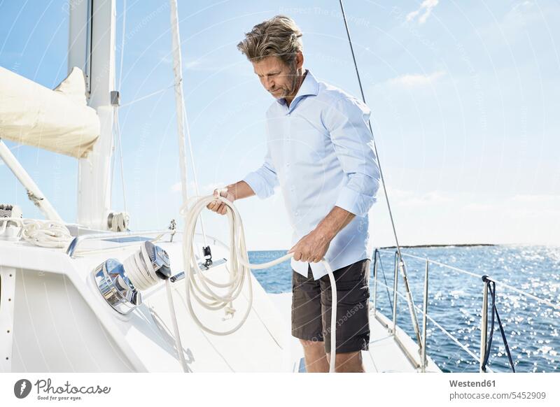 Mature man with rope on his sailing boat men males Adults grown-ups grownups adult people persons human being humans human beings boat sports sailor sailors Sea