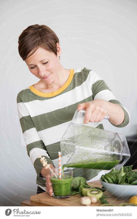 Smiling woman pouring green smoothie into a glass females women Smoothies Adults grown-ups grownups adult people persons human being humans human beings Drink