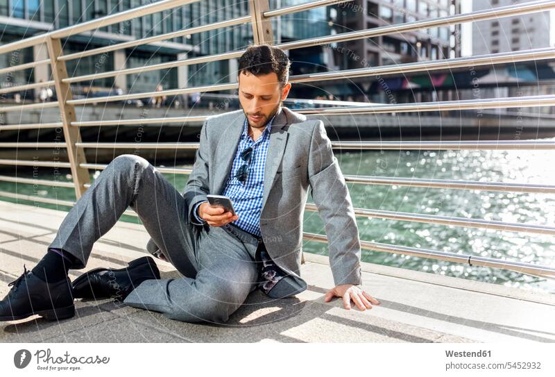 Businessman sitting on a bridge with cell phone in the city mobile phone mobiles mobile phones Cellphone cell phones Seated Business man Businessmen