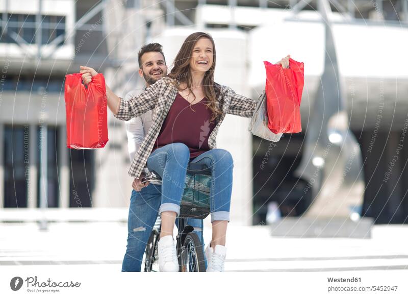 Happy young couple having fun in the city riding bicycle with shopping bags shopping-bag shopping-bags twosomes partnership couples laughing Laughter Fun funny