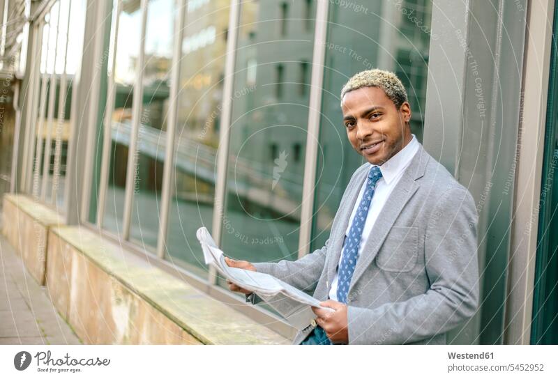 Businessman leaning against wall, reading newspaper standing Business man Businessmen Business men newspapers blond blond hair blonde hair business people