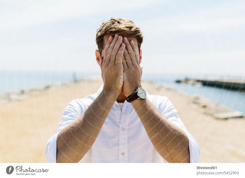 Mid adult man on the beach covering eyes men males portrait portraits eyes obscured Eyes covered Eye covered Hand Covering Eyes Covering eyes beaches hiding
