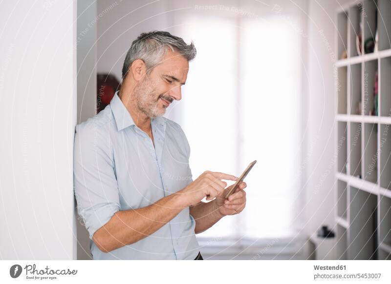Smiling mature man using cell phone at home use men males mobile phone mobiles mobile phones Cellphone cell phones smiling smile Adults grown-ups grownups adult