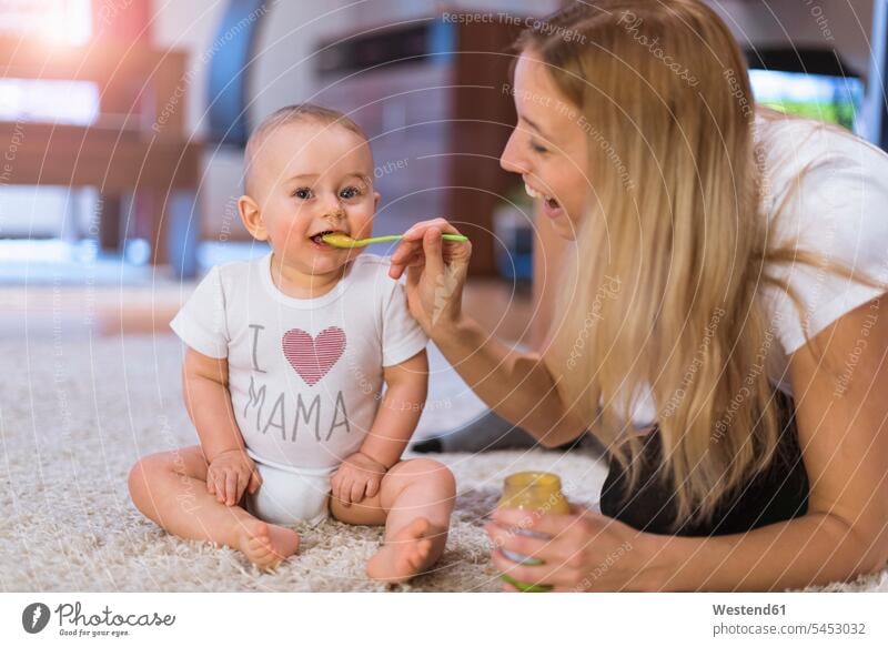 Mother feeding her baby son at home carpet carpets rug rugs sons manchild manchildren mother mommy mothers mummy mama infants nurselings babies eating floor