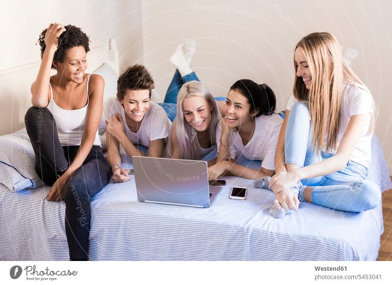 Happy female friends using laptop in bedroom beds happiness happy Domestic Bedroom woman females women Laptop Computers laptops notebook home at home mate