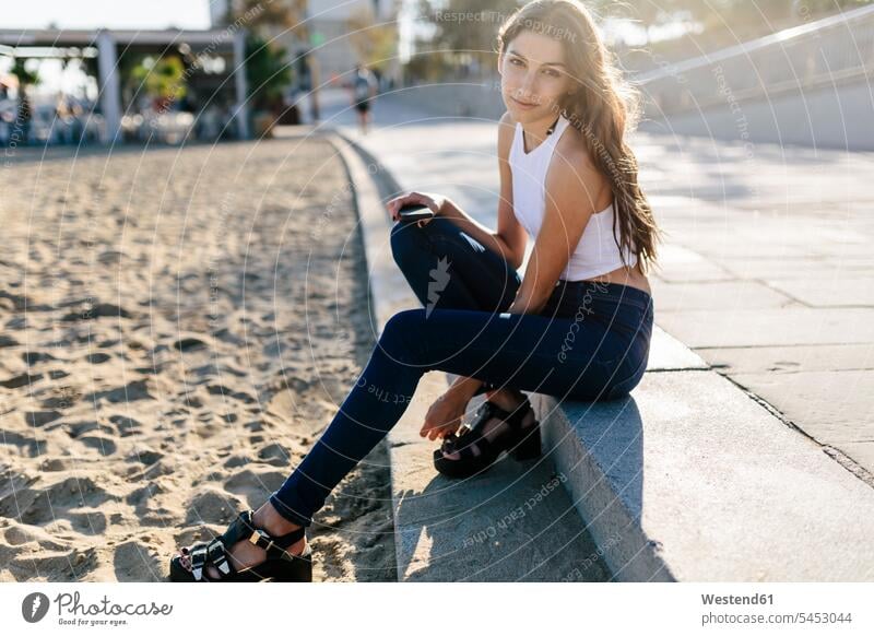 Portrait of young woman sitting on beach promenade at sunset females women sea front boardwalk Adults grown-ups grownups adult people persons human being humans