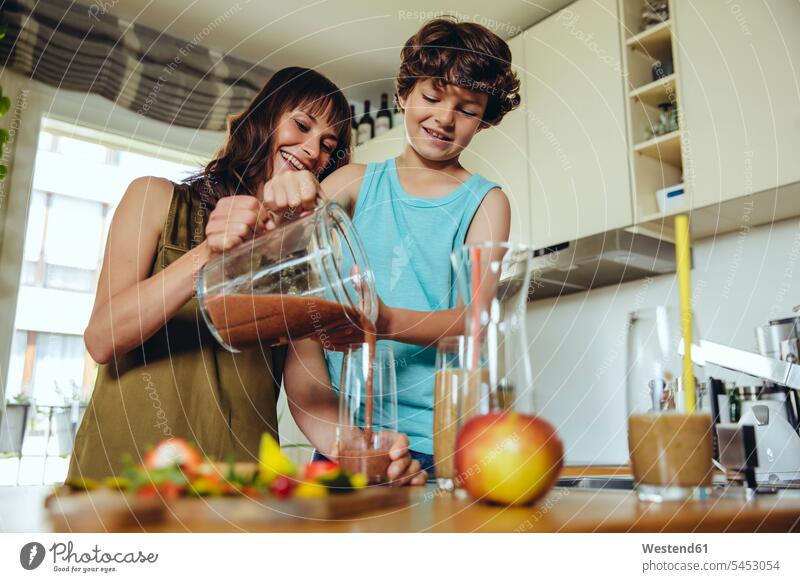 Mother and son pouring smoothie into glass Smoothies kitchen sons manchild manchildren mother mommy mothers mummy mama Drink beverages Drinks Beverage