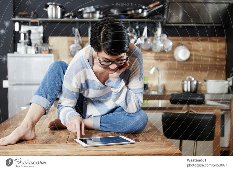Woman sitting on table in kitchen looking on tablet digitizer Tablet Computer Tablet PC Tablet Computers iPad Digital Tablet digital tablets woman females women