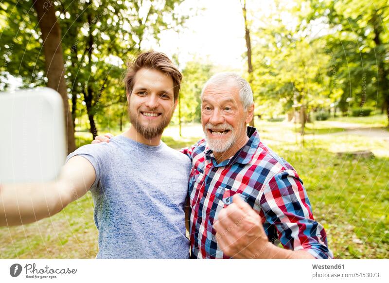 Portrait of senior father and his adult son taking selfie in a park Selfie Selfies fathers daddy dads papa parents family families people persons human being