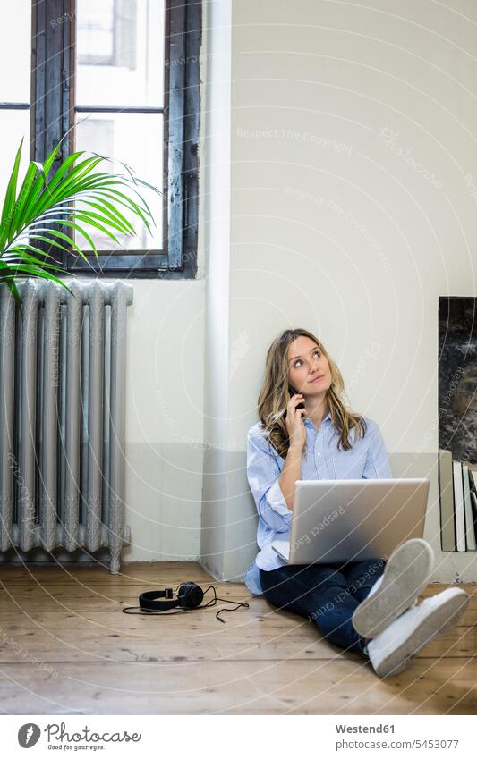 Woman sitting on the floor at home using cell phone and laptop Laptop Computers laptops notebook floors on the phone call telephoning On The Telephone calling