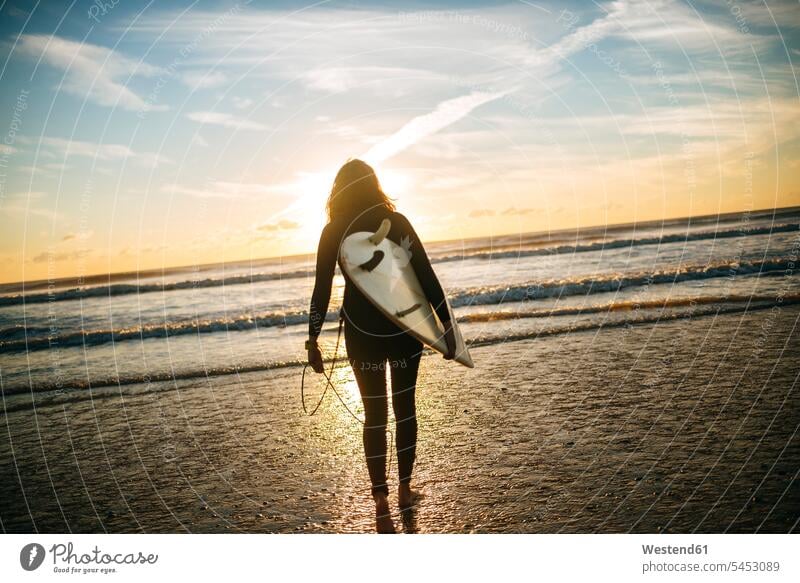 Back view of woman with surfboard on the beach by sunset surfboards surfer female surfer surfers female surfers surfing surf ride surf riding Surfboarding