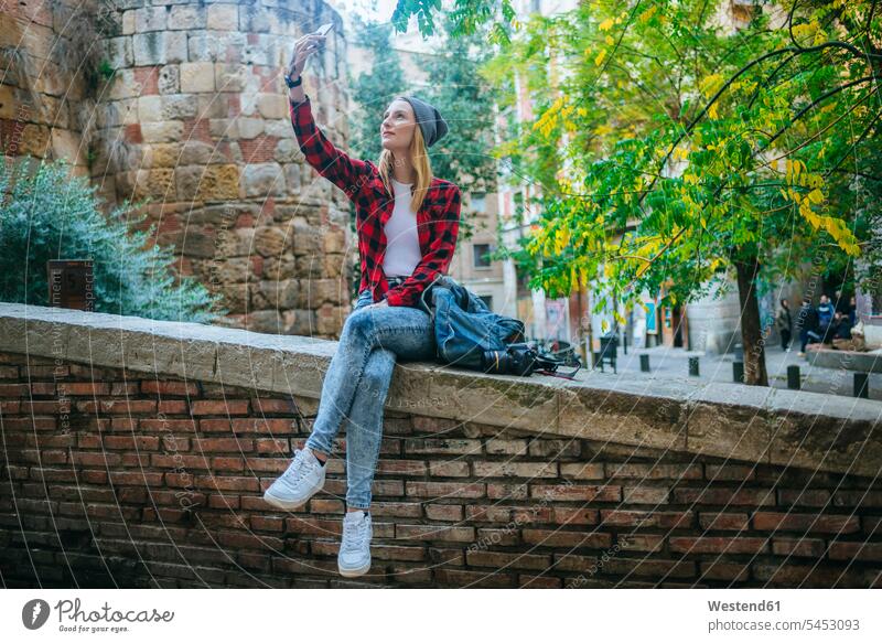 Spain, Barcelona, young woman sitting on a wall taking selfie with cell phone Selfie Selfies females women Adults grown-ups grownups adult people persons
