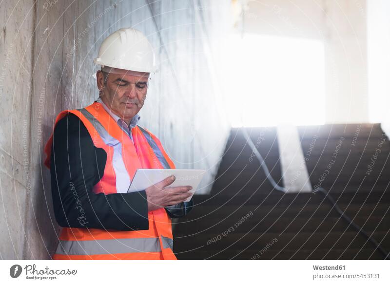 Man with tablet wearing safety vest in building under construction construction site Building Site sites Building Sites construction sites architect architects