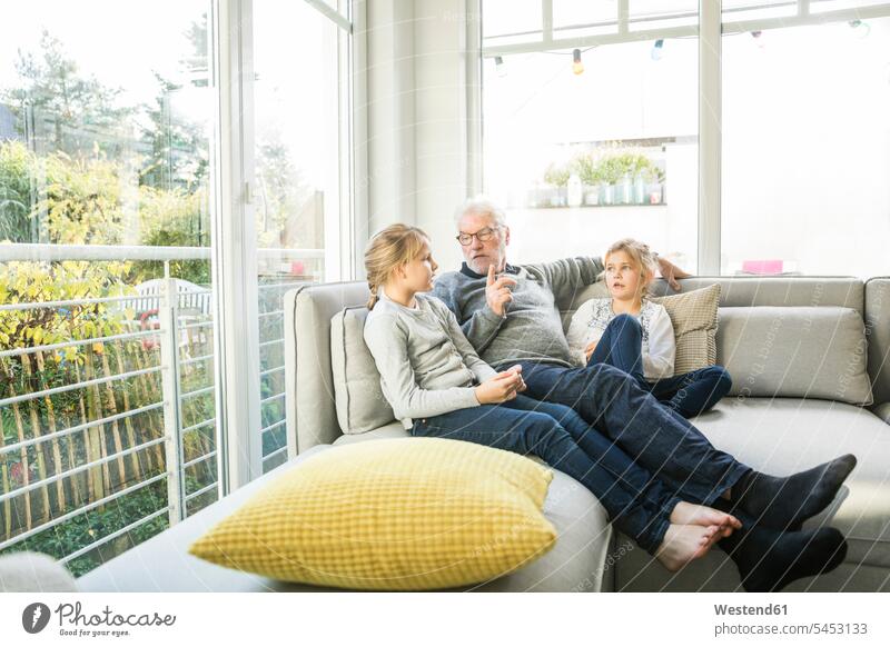 Grandfather talking to two girls on sofa in living room living rooms livingroom females couch settee sofas couches settees grandfather grandpas granddads