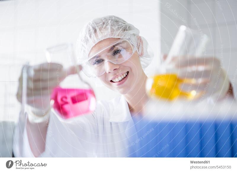 Smiling scientist in lab holding up two beakers with liquids smiling smile working At Work science sciences scientific Glass Beaker laboratory beaker