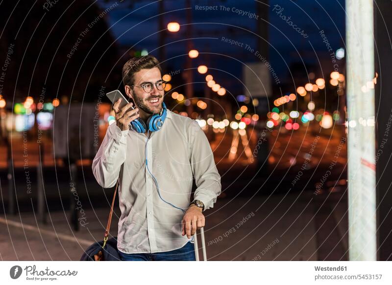 Young man in the city with headphones and cell phone at night men males headset town cities towns smiling smile mobile phone mobiles mobile phones Cellphone