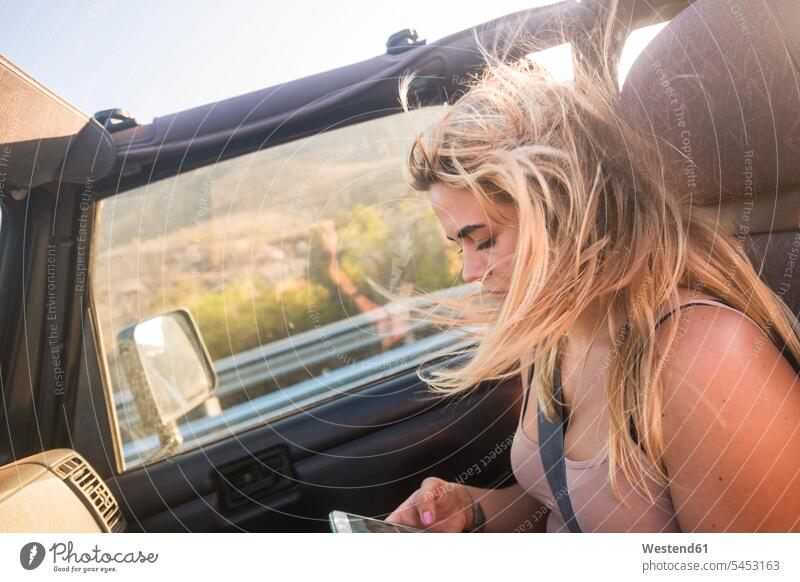 Blond woman with blowing hair sitting in car using cell phone use Smartphone iPhone Smartphones windswept Hair Blowing blowing hairs Seated blond blond hair