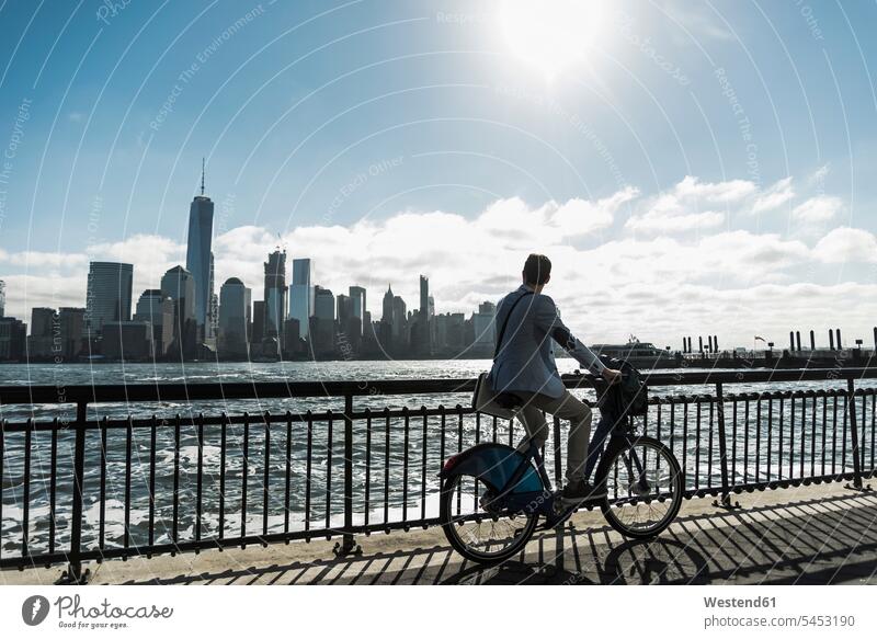 USA, man on bicycle at New Jersey waterfront with view to Manhattan driving drive New York State bikes bicycles Businessman Business man Businessmen