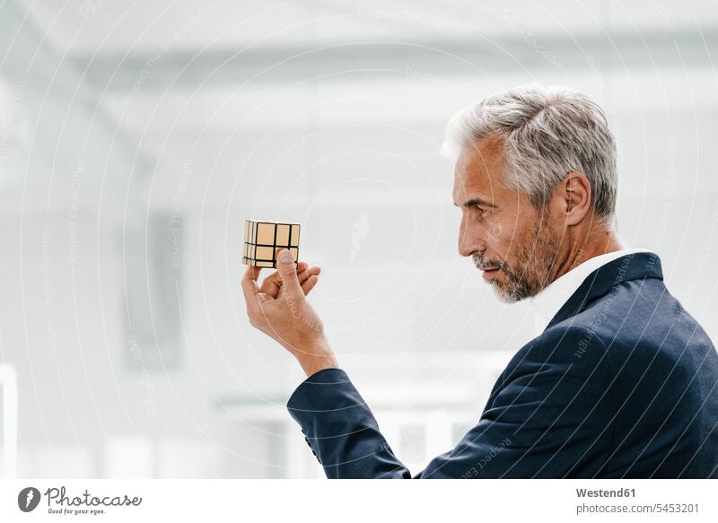 Mature businessman in office examining Rubik's Cube offices office room office rooms Businessman Business man Businessmen Business men workplace work place