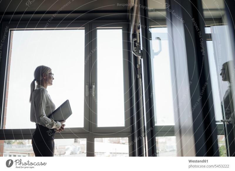 Businesswoman in office looking out of window businesswoman businesswomen business woman business women standing business people businesspeople business world