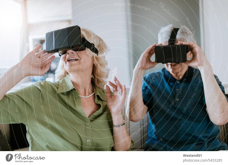 Senior couple at home sitting on couch wearing VR glasses twosomes partnership couples settee sofa sofas couches settees senior men senior man elder man