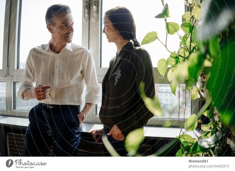 Businessman and businesswoman talking at the window Business man Businessmen Business men colleagues speaking businesswomen business woman business women