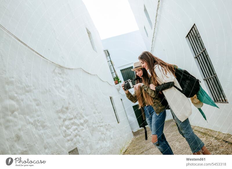 Two happy young women in a town looking at photos in a camera cameras female friends smiling smile mate friendship city cities towns woman females