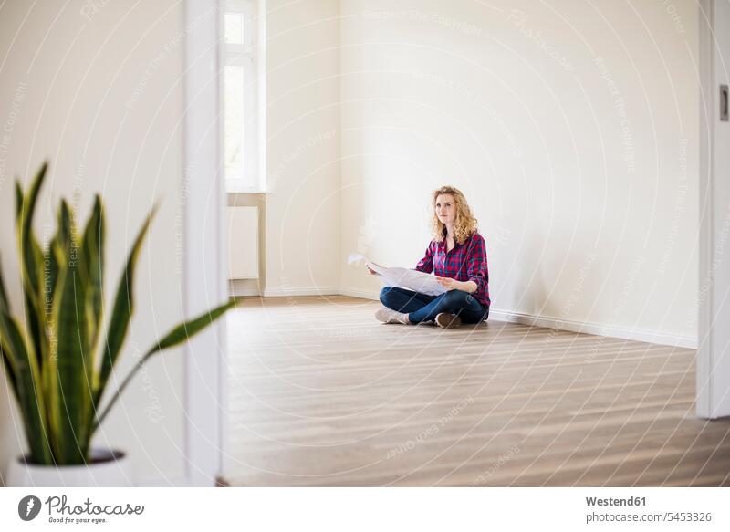 Young woman in new home sitting on floor with plan plans flat flats apartment apartments females women Adults grown-ups grownups adult people persons