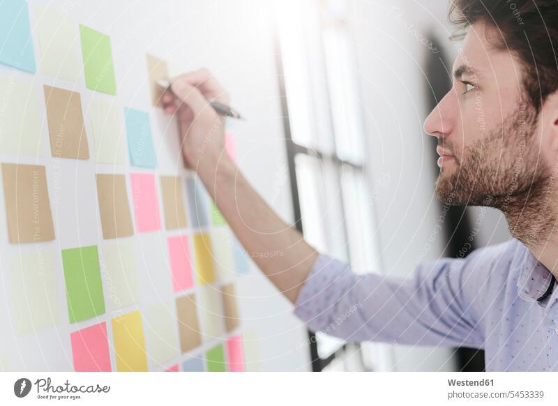 Young businessman working in office with sticky notes on wall strategy strategic Strategies writing write Adhesive Note post-it note adhesive notes Businessman
