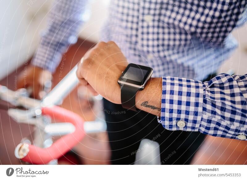 Close-up of man checking the smartwatch while holding a bike indoors Businessman Business man Businessmen Business men Checking The Time smart watch bicycle