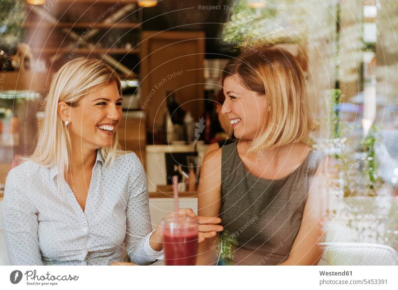 Two happy young women in a cafe laughing Laughter female friends Fun having fun funny talking speaking positive Emotion Feeling Feelings Sentiments Emotions
