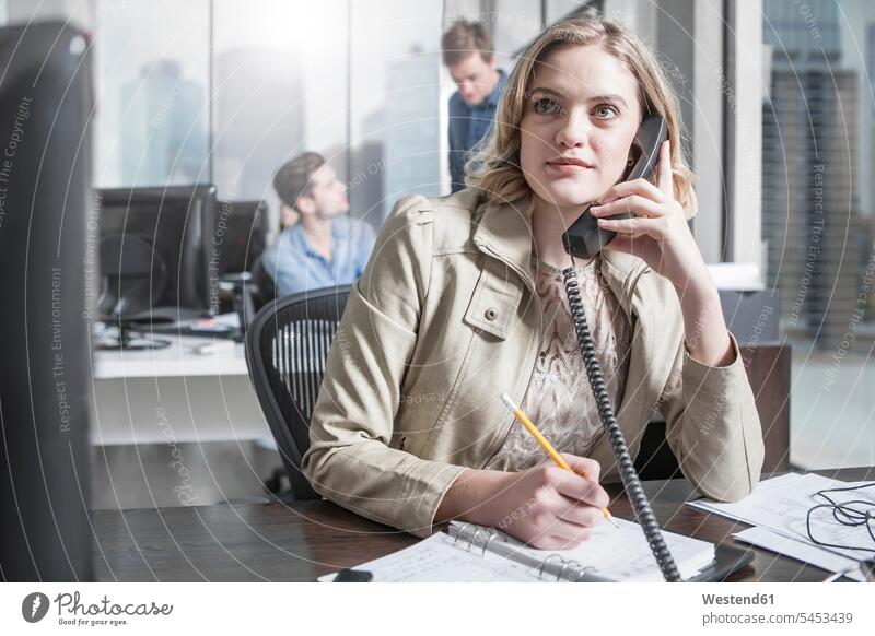 Young woman at desk in office on the phone females women offices office room office rooms call telephoning On The Telephone calling Adults grown-ups grownups