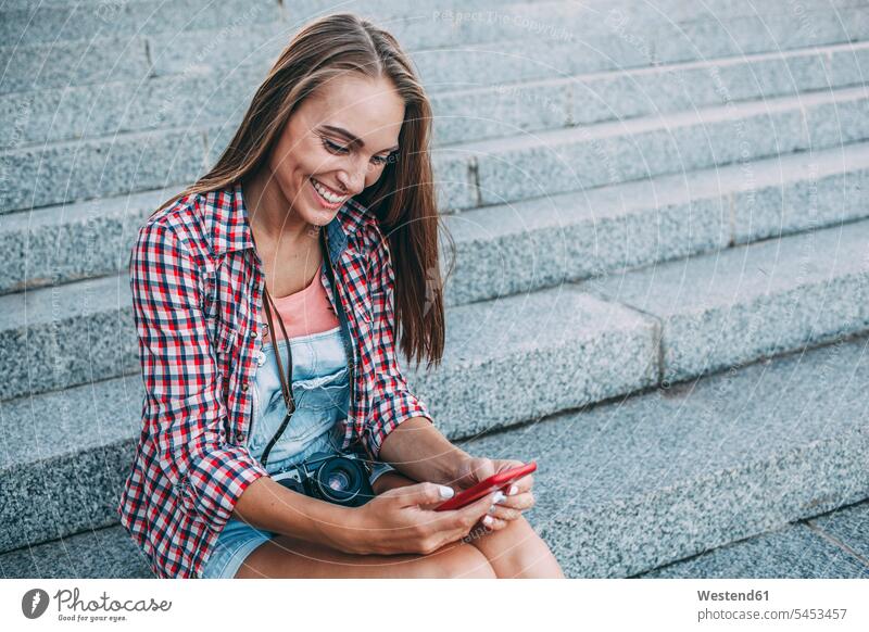 Smiling young woman sitting on stairs looking at cell phone mobile phone mobiles mobile phones Cellphone cell phones smiling smile females women stairway