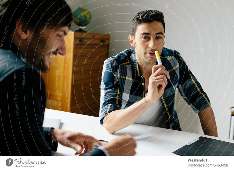 Two colleagues sitting at desk in office looking eyeing talking speaking offices office room office rooms smiling smile desks Businessman Business man