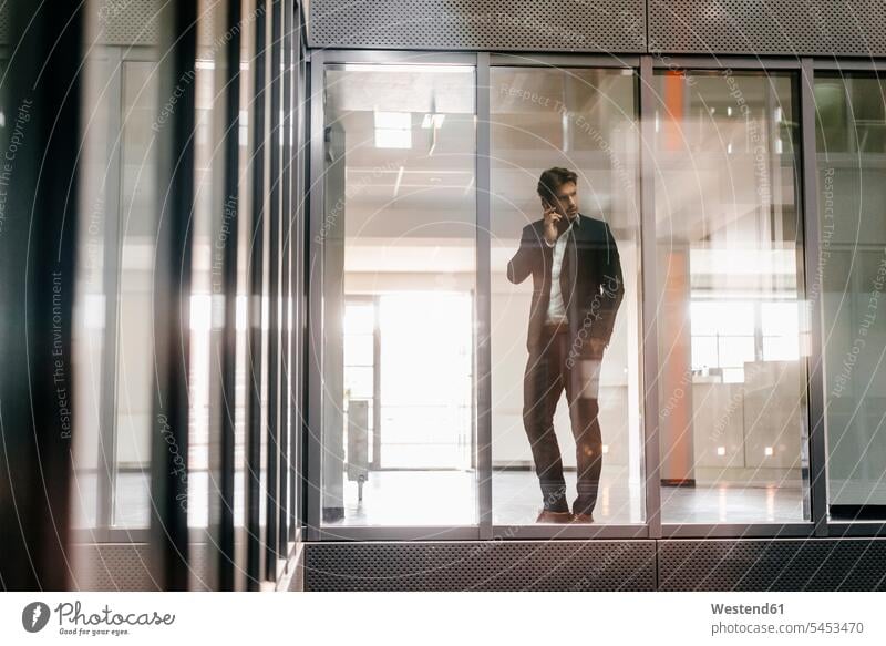 Businessman standing at window making a phone call Business man Businessmen Business men office offices office room office rooms glass pane glass panes