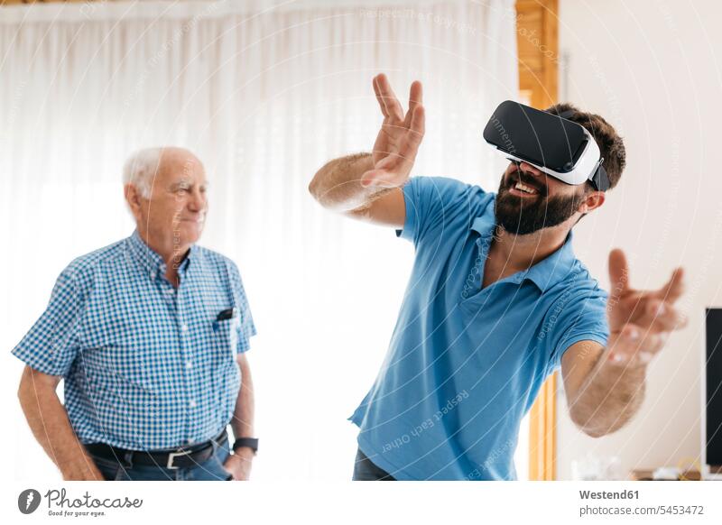 Smiling man using Virtual Reality Glasses at home while his grandfather watching him VR glasses Virtual-Reality Glasses virtual reality headset vr headset
