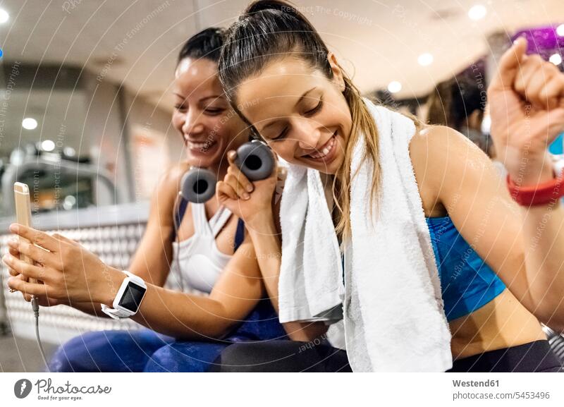 Two women having fun with their smartphone after work out in the gym break happiness happy exercising exercise training practising Sport Training mobile phone