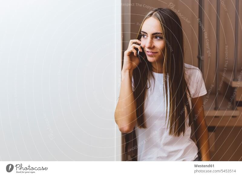 Smiling young woman at home on cell phone on the phone call telephoning On The Telephone calling smiling smile females women telephone call Phone Call