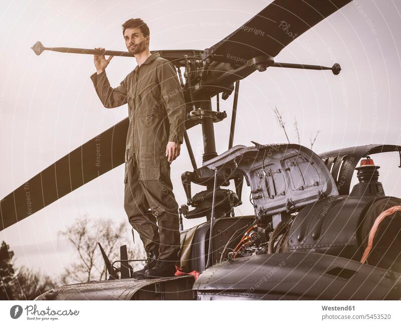 Man in overall standing on top of a helicopter pilot pilots aircraft Air Vehicle aircrafts Air Vehicles transportation man men males cool attitude composed
